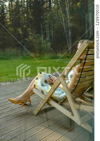 A view through the window at unrecognizable woman relaxing outdoors in a folding chair 128970010