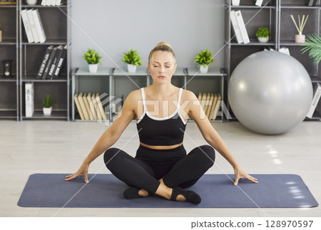 Yogi sporty fit woman sitting calmly relaxed on yoga mat in half lotus pose, meditating 128970597