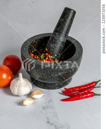 Granite Mortar and Pestle with Chillies Garlic and Tomatoes on Gray Surface Still Life 128971056