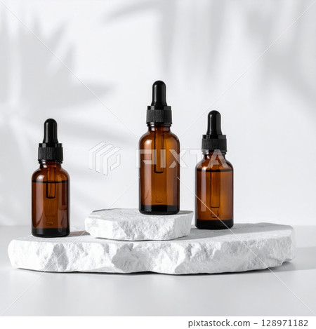 Three Amber Glass Dropper Bottles on White Stone Platform with Leaf Shadows Three Amber Glass Dropper Bottles on White Stone Platform with Leaf Shadows 128971182