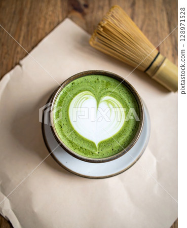 Matcha Latte with Heart Foam Art and Bamboo Whisk on Wooden Table Background 128971528