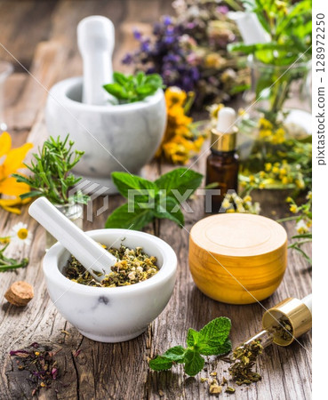 Assorted Herbs in Mortars with Essential Oils on Rustic Wood Surface in Soft Light 128972250