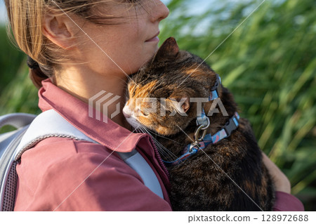 Scared cautious cat embrace woman on shoulder, hiding in new nature surroundings on walk together Scared cautious cat embrace woman on shoulder, hiding in new nature surroundings on walk together 128972688