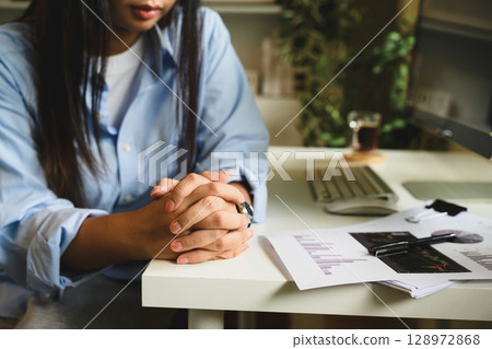 Serious businesswoman sitting at desk with folded hands, looking serious and concentrated 128972868