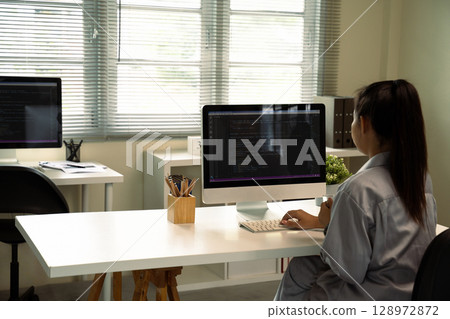 Female programmer coding on desktop computer in modern office Female programmer coding on desktop computer in modern office 128972872