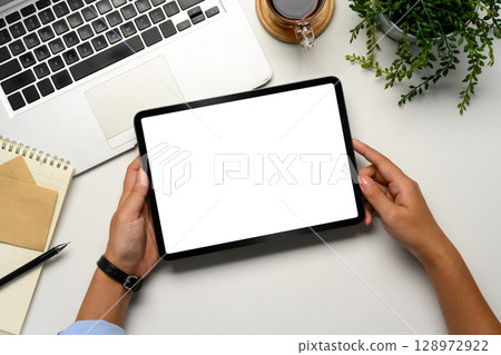 Top view of person holding digital tablet with empty white screen on a clean office desk Top view of person holding digital tablet with empty white screen on a clean office desk 128972922