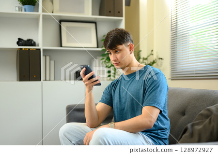 Man sitting comfortably on couch and checking messages on mobile phone 128972927