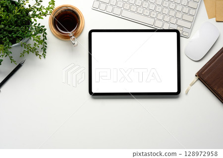 Top view of office desk with blank tablet screen, coffee cup, and green plant 128972958
