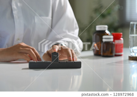 Close up of person organizing daily medication on desk. Health and medication concept Close up of person organizing daily medication on desk. Health and medication concept 128972968