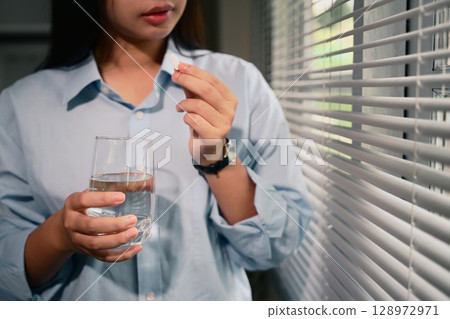 Young woman holding white tablet and a clear glass of water. Healthcare and wellness concept 128972971