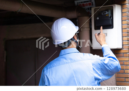 A man in work clothes inspecting an electric meter A man in work clothes inspecting an electric meter 128973680