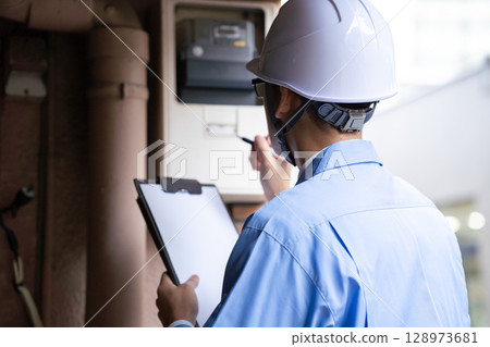 A man in work clothes inspecting an electric meter 128973681