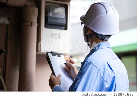 A man in work clothes inspecting an electric meter 128973682