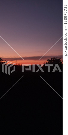 Dramatic Sunset Silhouette Over Hills Landscape with Warm Orange Glow, Moody Evening Sky, Dark Trees, Peaceful Rural Scene, Nature Photography. Dramatic Sunset Silhouette Over Hills Landscape with Warm Orange Glow, Moody Evening Sky, Dark Trees, Peaceful Rural Scene, Nature Photography. 128973733