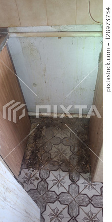 Dilapidated Bathroom Corner: Dirty Tile Floor, Wall Damage, Debris Accumulation, Rusty Elements, Brown, Beige and White Color Scheme. Dilapidated Bathroom Corner: Dirty Tile Floor, Wall Damage, Debris Accumulation, Rusty Elements, Brown, Beige and White Color Scheme. 128973734