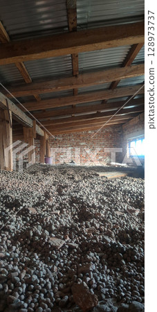 Abandoned Brick Building Interior with Gravel Floor. Rustic Wood Roof, Dark Shadows, Vintage Architecture, Dilapidated Structure, Natural Light. 128973737