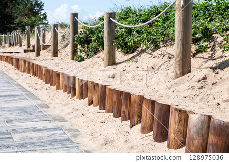 Coastal Footpath with Wooden Barrier and Rope Fence Along Sandy Dune Landscape by the Sea 128975036