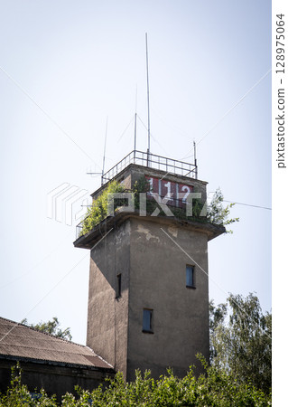 Abandoned Concrete Tower with Emergency Number 112 and Overgrown Vegetation on Rooftop 128975064