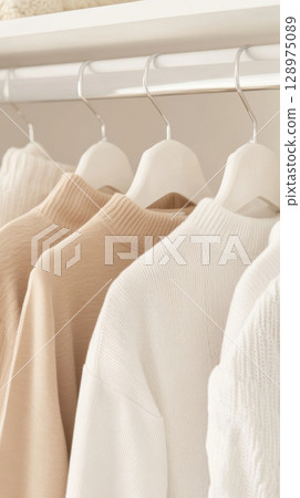 Neutral clothes hanging on a rail in a bright, organized closet, background 128975089