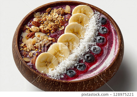 Delicious smoothie. Colorful acai bowl with banana slices, coconut flakes and granola on a white background. Healthy and Wellness Breakfast for luxury resorts. Delicious smoothie. Colorful acai bowl with banana slices, coconut flakes and granola on a white background. Healthy and Wellness Breakfast for luxury resorts. 128975221