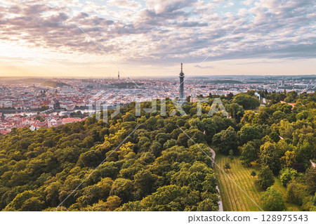 Petrin Lookout Tower stands majestically atop a hill in Prague during sunrise. The golden light fills the sky, illuminating the city and its surrounding greenery, creating a breathtaking view. Petrin Lookout Tower stands majestically atop a hill in Prague during sunrise. The golden light fills the sky, illuminating the city and its surrounding greenery, creating a breathtaking view. 128975543