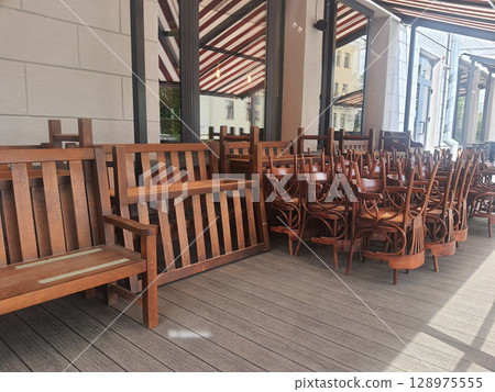 Closed cafe with wooden chairs and benches stacked on the terrace 128975555