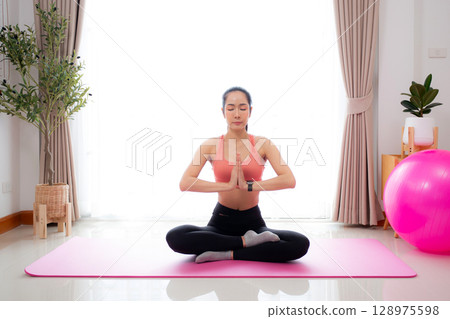 Young asian woman meditation sitting on mat in serene and tranquility with yoga in living room. Young asian woman meditation sitting on mat in serene and tranquility with yoga in living room. 128975598