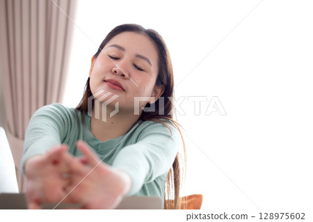 Young asian businesswoman sitting on sofa taking a break after overworked with stretching arm. Young asian businesswoman sitting on sofa taking a break after overworked with stretching arm. 128975602