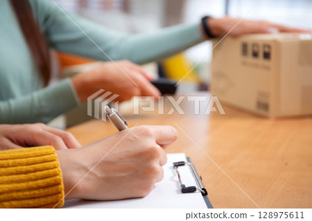 Closeup hand woman writing document while scanning package with barcode reader. Closeup hand woman writing document while scanning package with barcode reader. 128975611