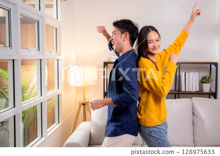 Young asian couple dancing playful together in cozy living room at home, smile and enjoy. Young asian couple dancing playful together in cozy living room at home, smile and enjoy. 128975633