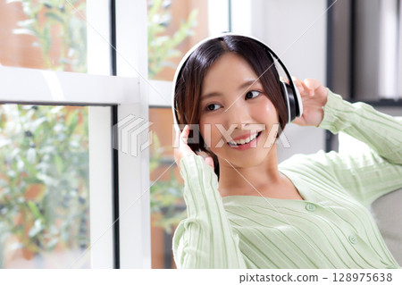 Happy young asian woman wearing headphones listening music while sitting on sofa with fun. Happy young asian woman wearing headphones listening music while sitting on sofa with fun. 128975638