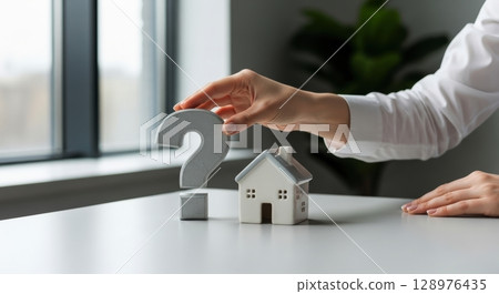 Woman hand placing question mark next to a miniature house, symbolizing real estate questions. 128976435