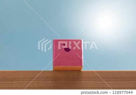 Smiling wooden block sits under a bright blue sky, expressing happiness and serenity. Positive mental health and emotional wellbeing 128977044