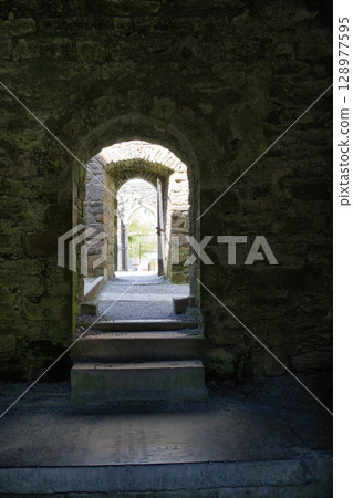 A series of stone archways in an old Irish castle, leading to an open doorway, with steps. A series of stone archways in an old Irish castle, leading to an open doorway, with steps. 128977595