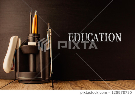 A pencil holder with pencils and a pen sits on a wooden table 128978750