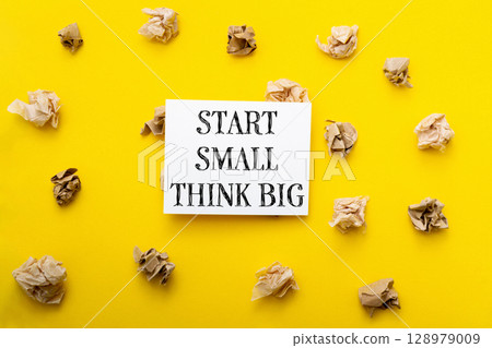 A yellow background with a white sign that says Start small, think big A yellow background with a white sign that says Start small, think big 128979009