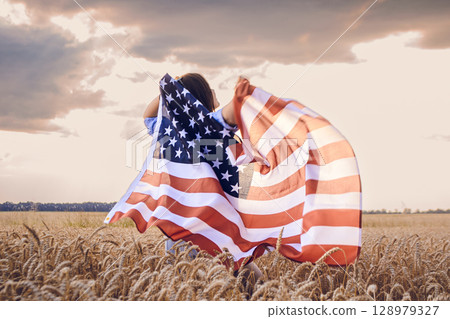 Woman is holding a large American flag in a field 128979327