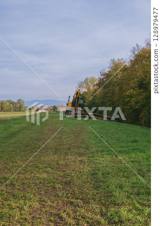Tractor is in the middle of a field with a cloudy sky in the background Tractor is in the middle of a field with a cloudy sky in the background 128979477