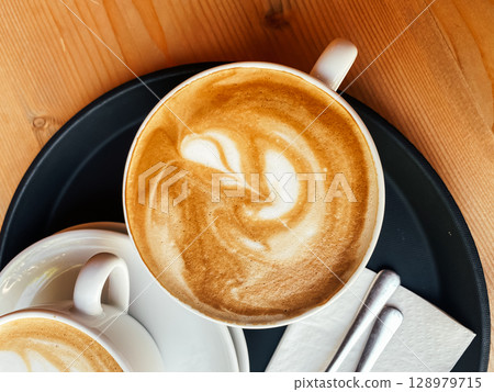 Cup of coffee with a swirl of cream on top sits on a tray Cup of coffee with a swirl of cream on top sits on a tray 128979715