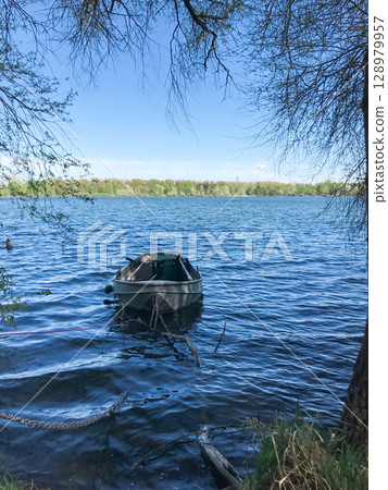 A small boat is floating in the water near a tree 128979957