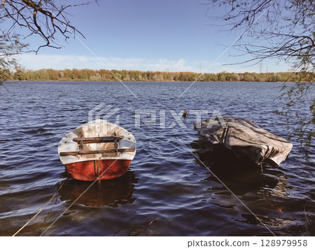 Two boats are floating in a lake, one of which is covered with a tarp 128979958