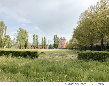 A large red building sits in a field with trees and grass A large red building sits in a field with trees and grass 128979970