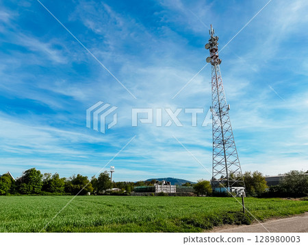 A tall tower with a white top stands in a field, featuring antennas for 5G A tall tower with a white top stands in a field, featuring antennas for 5G 128980003