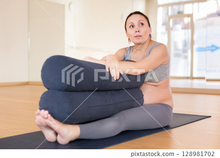 pregnant woman practices yoga with roll in hall pregnant woman practices yoga with roll in hall 128981702
