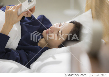 一名婦女在床上的看一個智能手機 一名婦女在床上的看一個智能手機 128981966