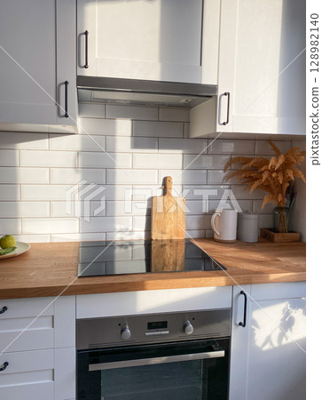 Stylish kitchen with electric stove, wooden countertop and white cabinets, filled Stylish kitchen with electric stove, wooden countertop and white cabinets, filled 128982140