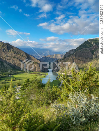 Landscape with beautiful river flowing through green valley and rocky mountains in natural daylight 128982143