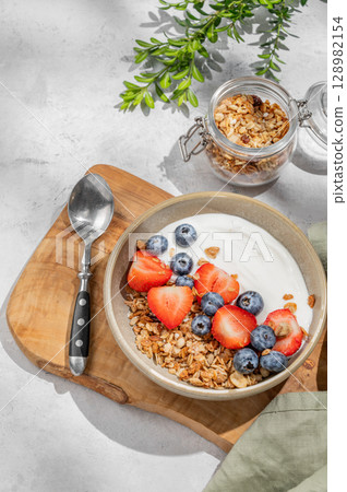 Natural yogurt with granola, blueberry and strawberry in a bowl on a wooden board 128982154