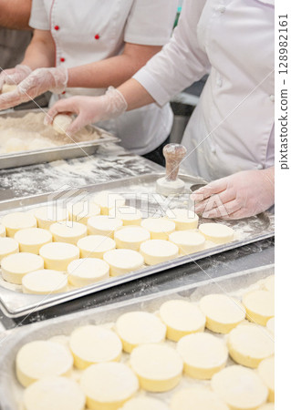 Chefs in uniform prepare cottafe cheese or syrniki on metal trays sprinkled with flour  128982161