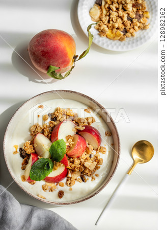 Natural greek yogurt with granola or muesli, peach and mint in a bowl on a white background 128982162